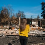 woman looking at wildfire destroyed home